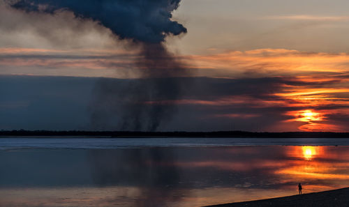 Smoke emitting over lake against sky during sunset