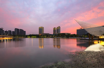 Lake by buildings against sky during sunset