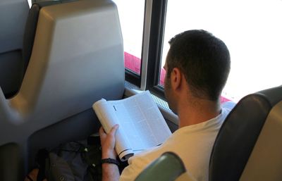 Man reading book while sitting in bus