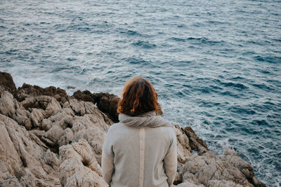 Rear view of woman sitting on rock by sea