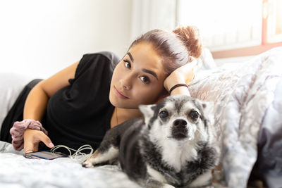 Portrait of young woman with dog lying on bed at home