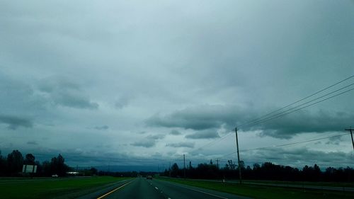 Road passing through field against cloudy sky