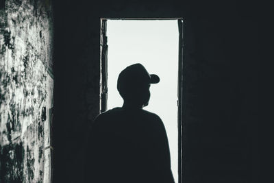 Silhouette boy standing by window in darkroom