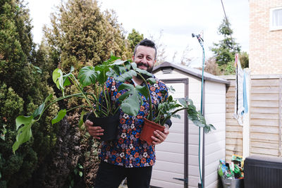 Smiling man with potted plants standing in back yard