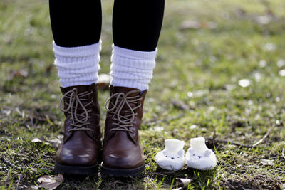 Low section of woman standing by baby boots on field