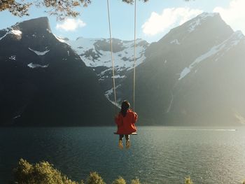 Woman swinging over calm lake against mountain range