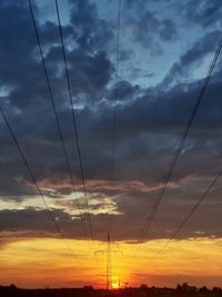 Low angle view of silhouette power lines against dramatic sky during sunset