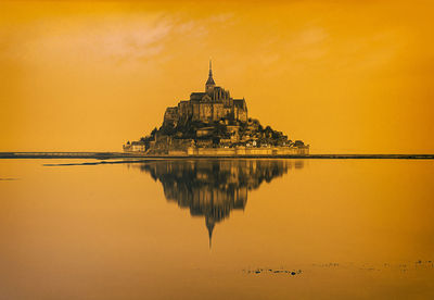 Reflection of building on water against orange sky