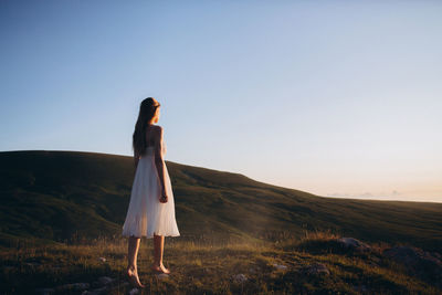 Young woman standing at field against clear sky