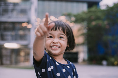 Smiling cute girl pointing while standing outdoors