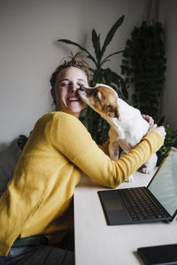 Smiling woman playing with dog while sitting at home office