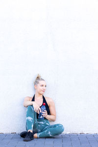 Portrait of young woman sitting against wall