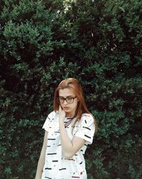 Portrait of young woman standing against trees