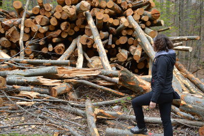 Side view full length of woman standing by logs at forest