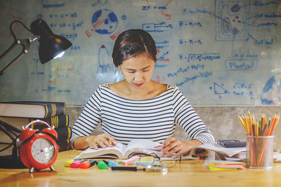 Woman studying at desk against whiteboard