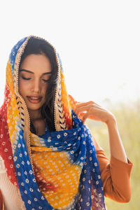 Young ethnic indian female in traditional colorful headscarf with eyes closed while standing against blurred tropical yard