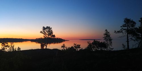 Silhouette trees by lake against sky during sunset