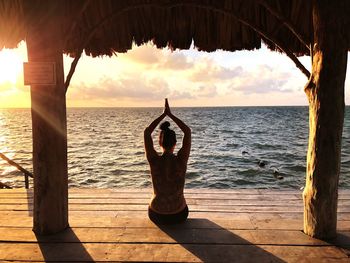 Rear view of woman sitting on pier over sea against sky during sunset