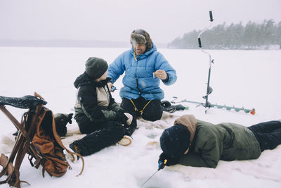 Happy man talking with son while friend fishing lying on snow