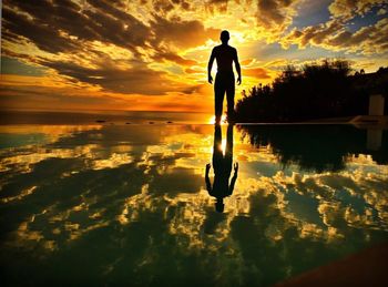 Silhouette man standing by sea against sky during sunset