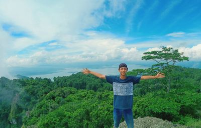 Cheerful young man with arms outstretched standing against forest