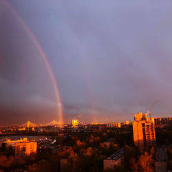 Rainbow over city buildings against sky during sunset