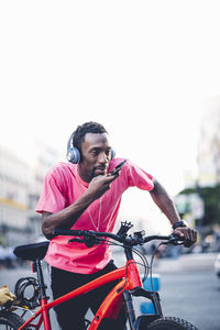 Young man with e bike and headphones using smartphone in the city