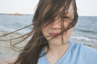 Close-up portrait of girl standing at beach against sky