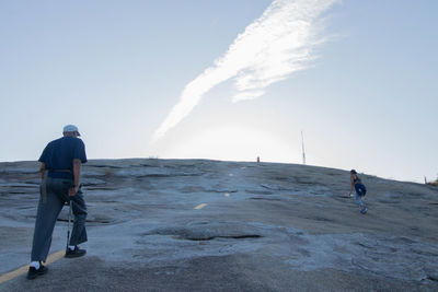 Rear view of men walking on beach against clear sky