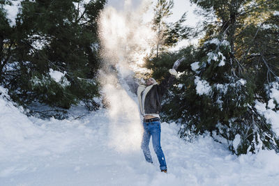 Cheerful man playing with snow against trees