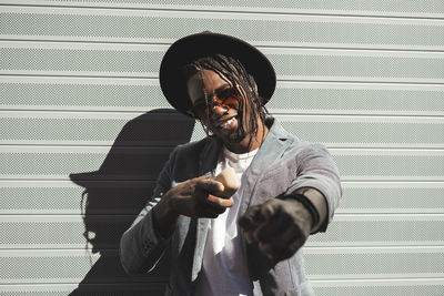 Portrait of smiling man pointing while standing against corrugated wall