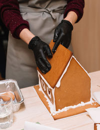 The process of making a gingerbread house, gluing the ginger roof with icing, squeezing tight