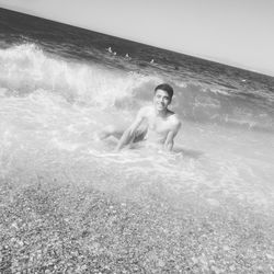 Full length of shirtless man in sea against sky