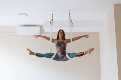 Mid adult sportswoman with arms outstretched doing splits at yoga studio