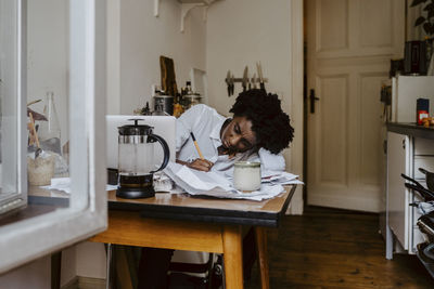 Female entrepreneur writing on document while working in living room at home