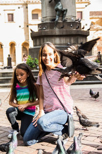 Smiling mother feeding pigeons with daughter in city