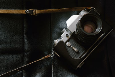 Old retro photo camera with lens on black leather background