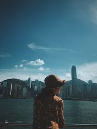 Rear view of woman standing by sea against buildings in city