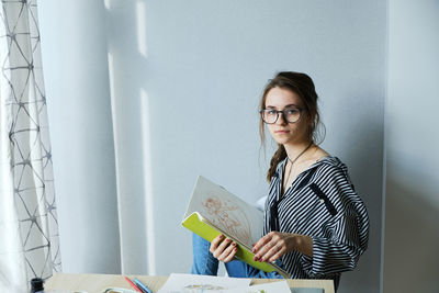 Millennial girl draws fabulous images on paper while sitting at home