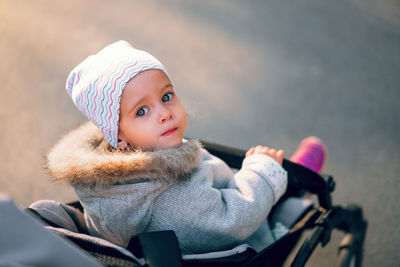 Portrait of cute girl sitting in baby stroller during winter