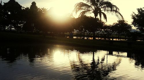 Silhouette trees by lake against sky during sunset