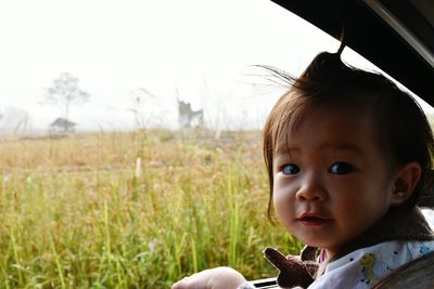 Portrait of cute baby girl in car against field