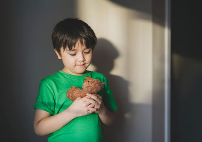 Boy holding toy while standing against wall at home