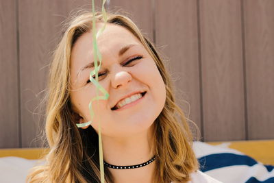 Cheerful woman with closed eyes holding balloon against wall