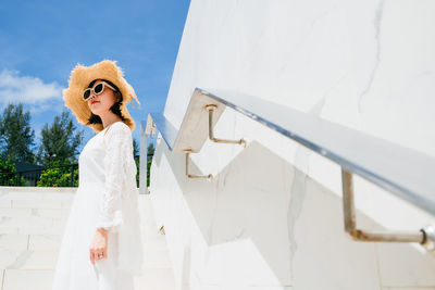 Woman wearing sunglasses standing against white wall