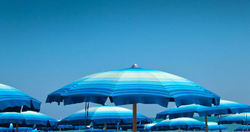 Low angle view of parasols against clear blue sky