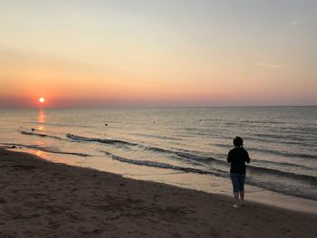 Rear view of woman standing on beach during sunset