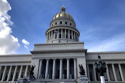 Low angle view of havana capitol and cuban flag against cloudy sky