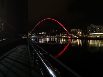 Illuminated bridge over river by buildings in city at night