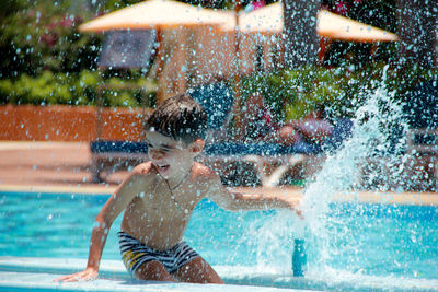 Boy enjoying by fountain in swimming pool on sunny day